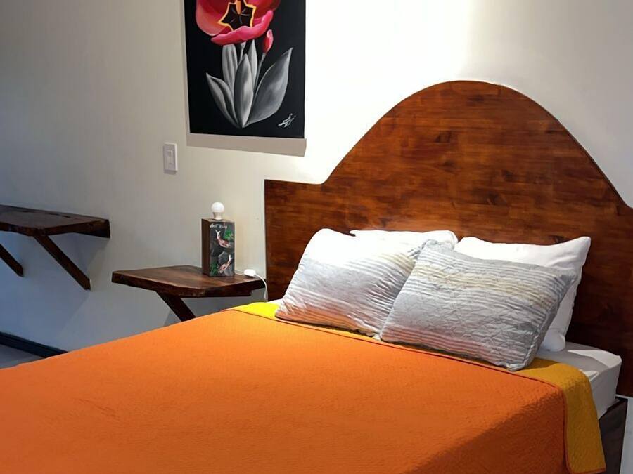 Une chambre à coucher avec une tête de lit en bois, une grande couvre-lit orange, des oreillers blancs et une table de chevet avec une lampe.