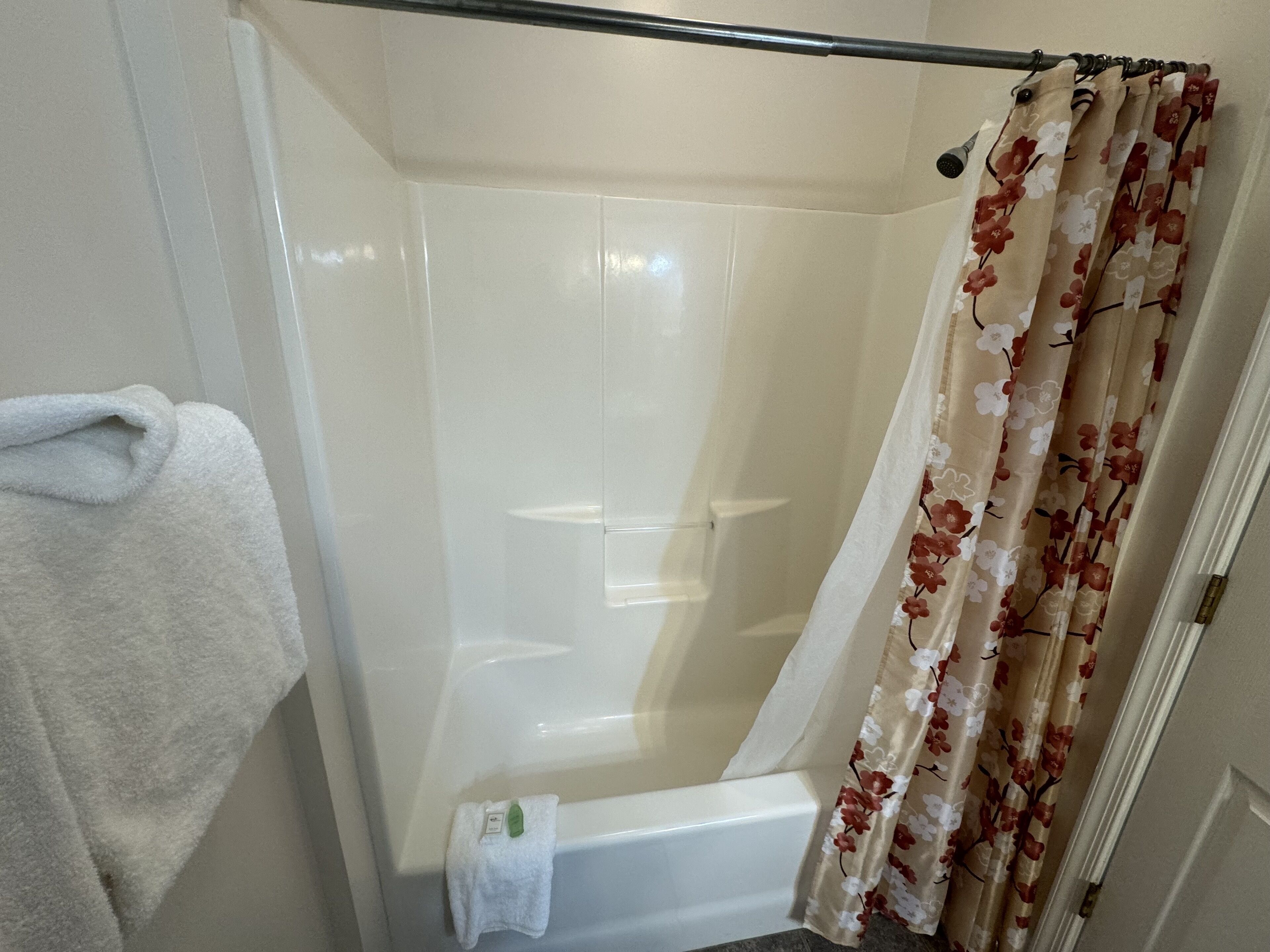 A bathroom with a white bathtub, a shower curtain with a floral pattern, and a white towel hanging on the wall.