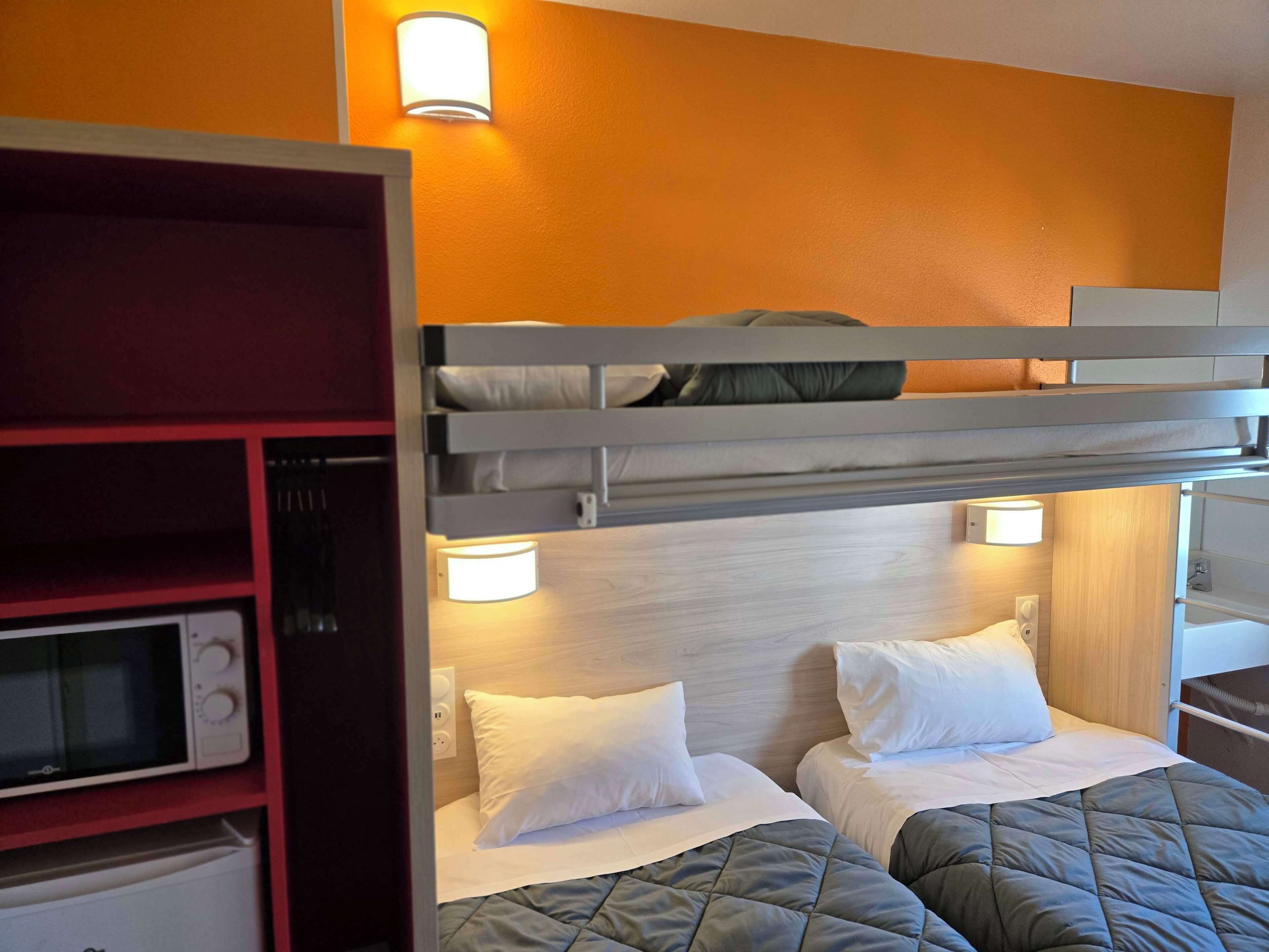 A hotel room with a bunk bed, a microwave, a red shelf, and two bedside lamps.