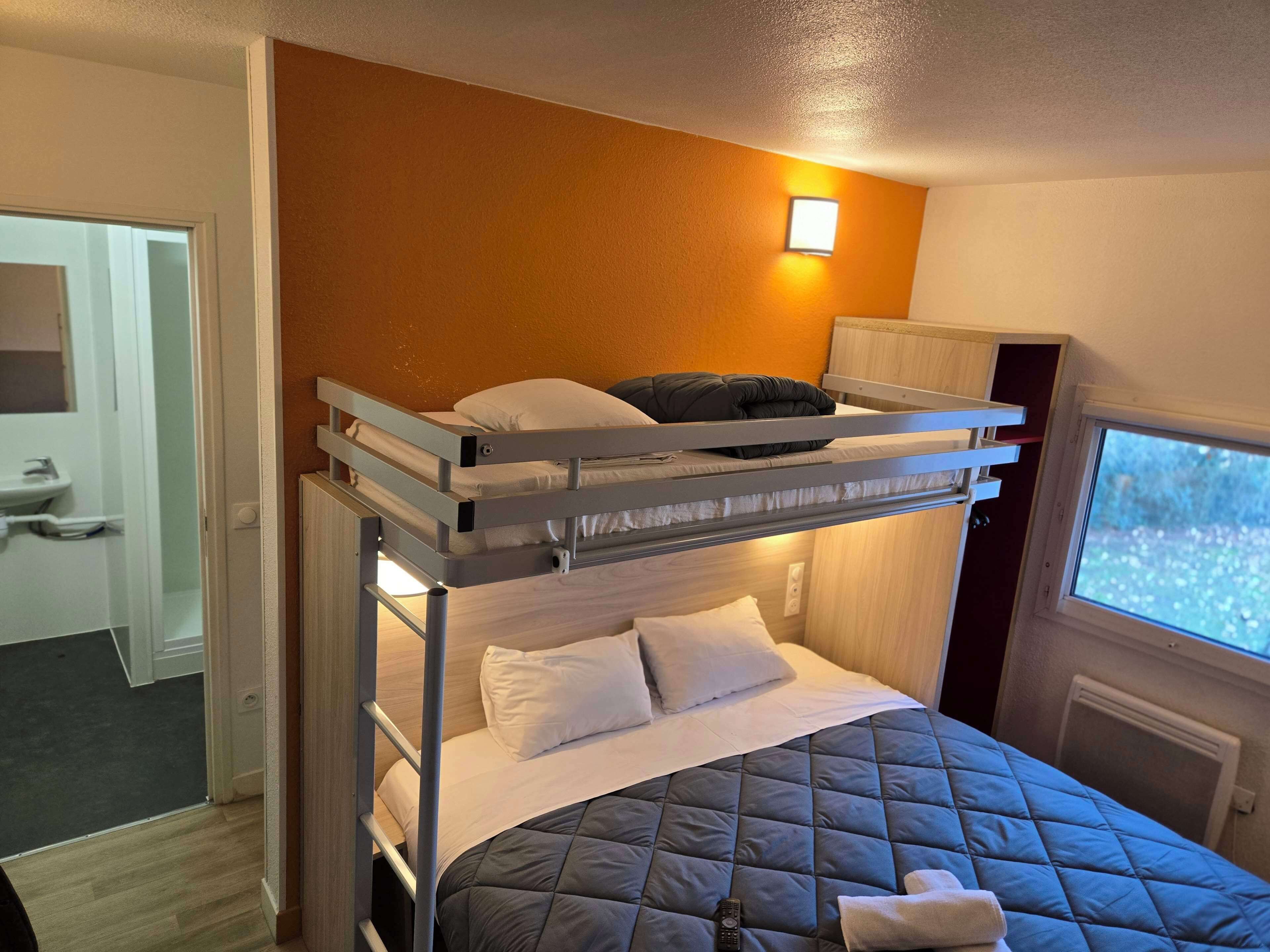 Une chambre avec un lit superposé, une fenêtre, une table de chevet et un petit placard.