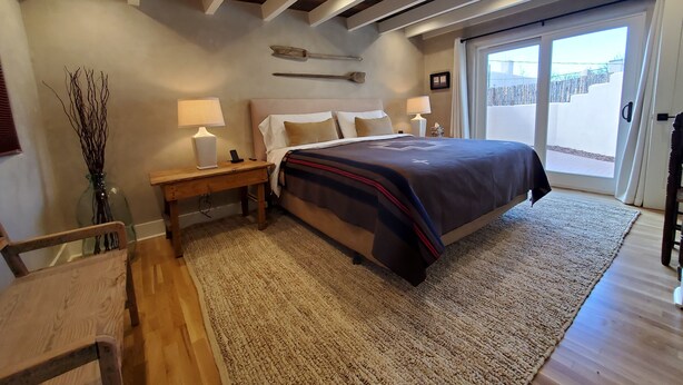 A bedroom with a bed, bedside tables, a lamp, a vase with branches, and a view through a sliding door. - Quiet retreat near Plaza (Santa Fe)