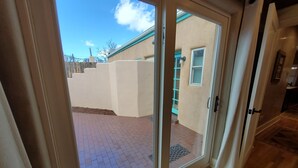 A sliding glass door leading to a patio with a brick floor and a view of a building with a light-colored exterior and a window. - Quiet retreat near Plaza (Santa Fe)