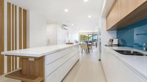 A modern kitchen with a central island, wooden accents, and a view to the dining area. - Salt Yeppoon (Yeppoon)
