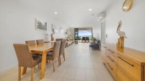 A spacious dining area with a wooden table and chairs, a sofa, and a wooden cabinet with decorative items. - Salt Yeppoon (Yeppoon)