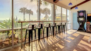 A bar area with a view of palm trees and a beach, featuring bar stools and a dart game machine. - Beachfront Studio - Sleeps 4 (Daytona Beach)