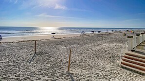 A beach with a wooden walkway leading to the water, a sandy beach, and umbrellas. - Beachfront Studio - Sleeps 4 (Daytona Beach)