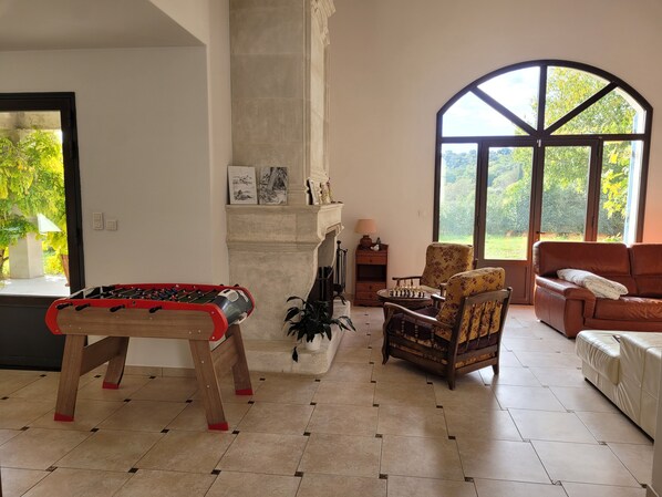 A spacious living room with a foosball table, a chessboard, a sofa, and a large window offering a view of greenery. - Villa “Des Oliviers” – perfect for a visit to Provence (Caumont-sur-Durance)