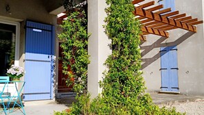 A building with a blue door and window, a wooden pergola, and a table with chairs outside. - Villa des oliviers ideal for visiting Provence (Caumont-sur-Durance)
