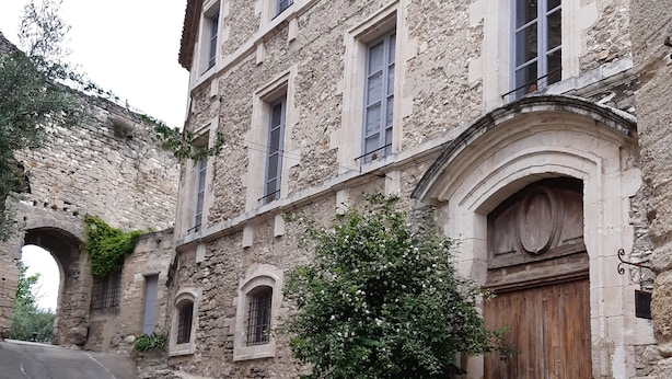 A historic stone building with a large wooden door, arched windows, and a stone archway. - Villa des oliviers ideal for visiting Provence (Caumont-sur-Durance)
