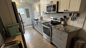 A modern kitchen with stainless steel appliances, wooden flooring, and white cabinetry. - Remodeled Jamestown beach cottage within walking distance to beach (Jamestown)