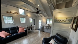 A spacious living area with a black leather sofa, a dining table with chairs, and a kitchen area. - Remodeled Jamestown beach cottage within walking distance to beach (Jamestown)