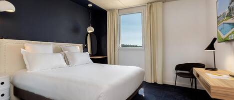 A hotel room with a large bed, a desk, a chair, a lamp, and a window with curtains.