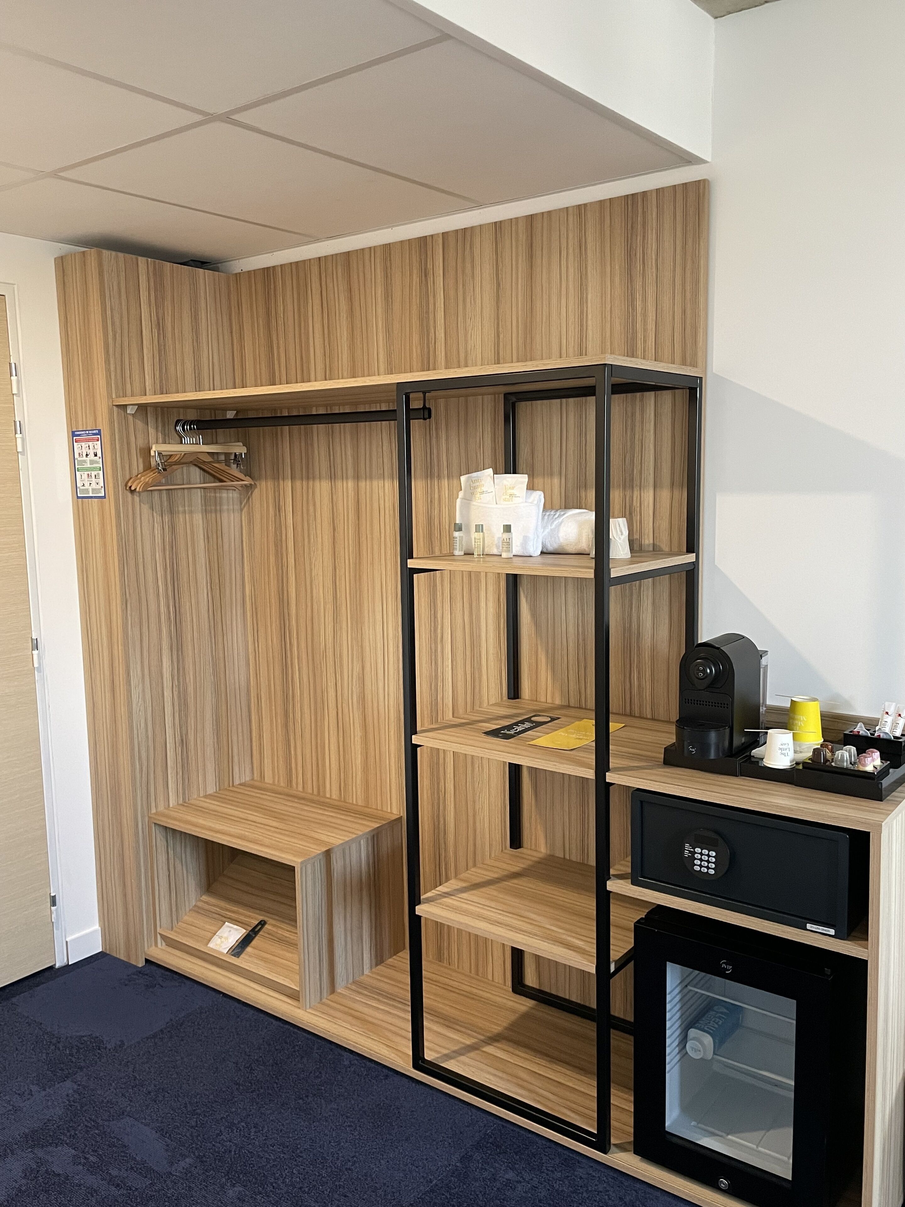 A compact room with a wooden wardrobe, a small kitchenette, and a built-in mini-fridge.