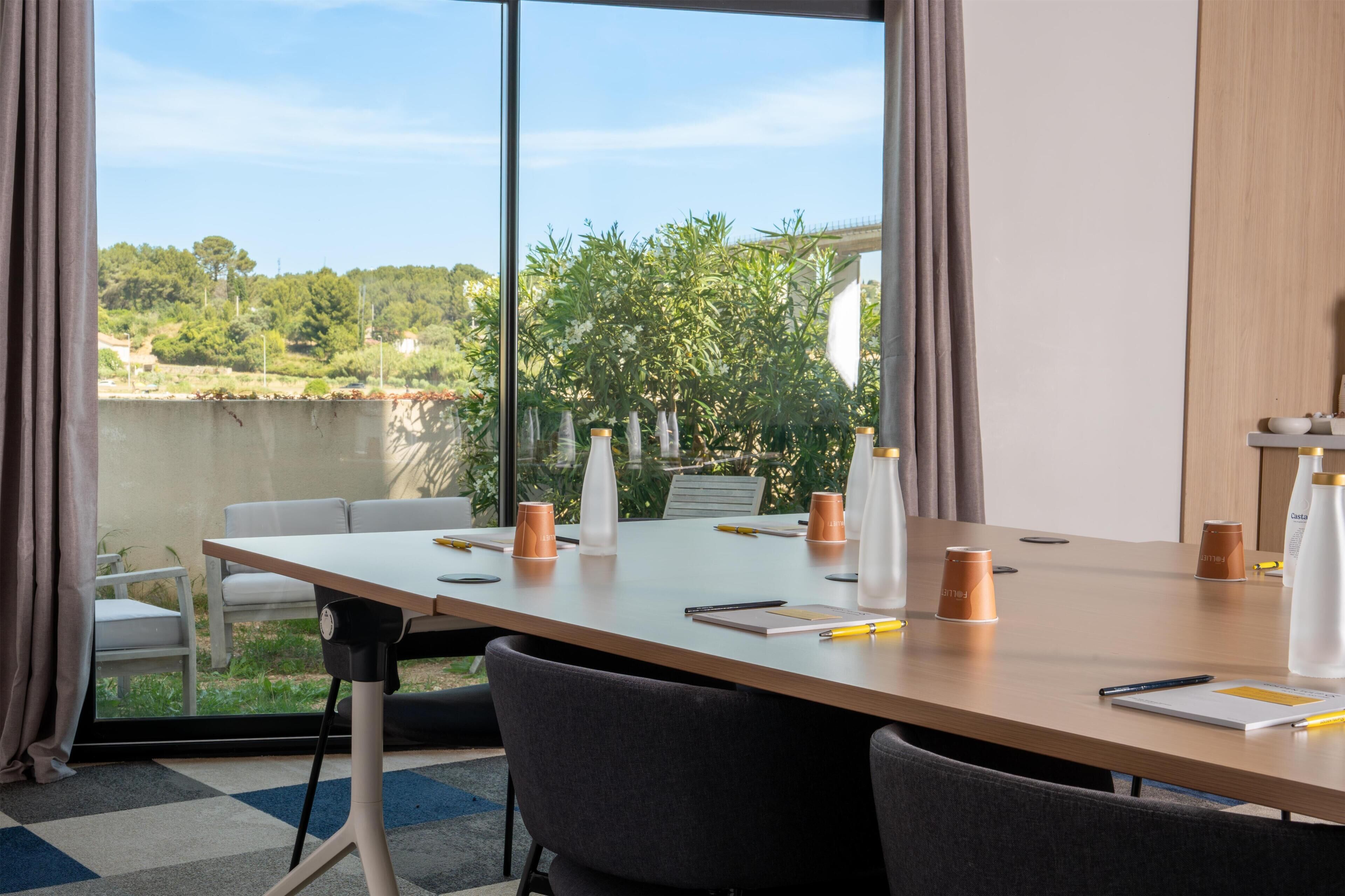 Une salle de conférence dotée d’une longue table, de chaises et offrant une vue sur la verdure environnante.
