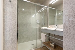Un baño moderno con ducha de vidrio, tocador con espejo y repisa de madera.