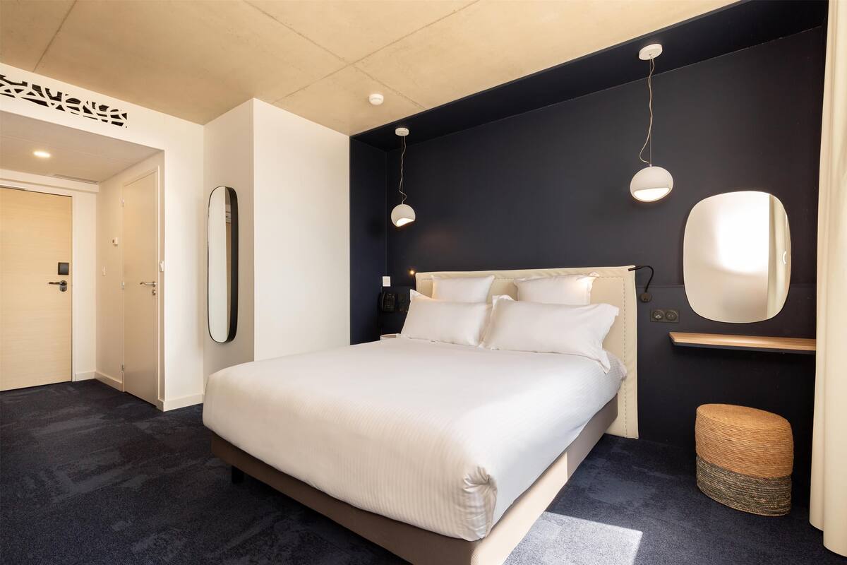 A modern bedroom with a large bed, a bedside table, a mirror, and two pendant lights.