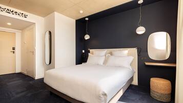 Une chambre moderne avec un grand lit, une table de chevet, un miroir et deux lampes suspendues.