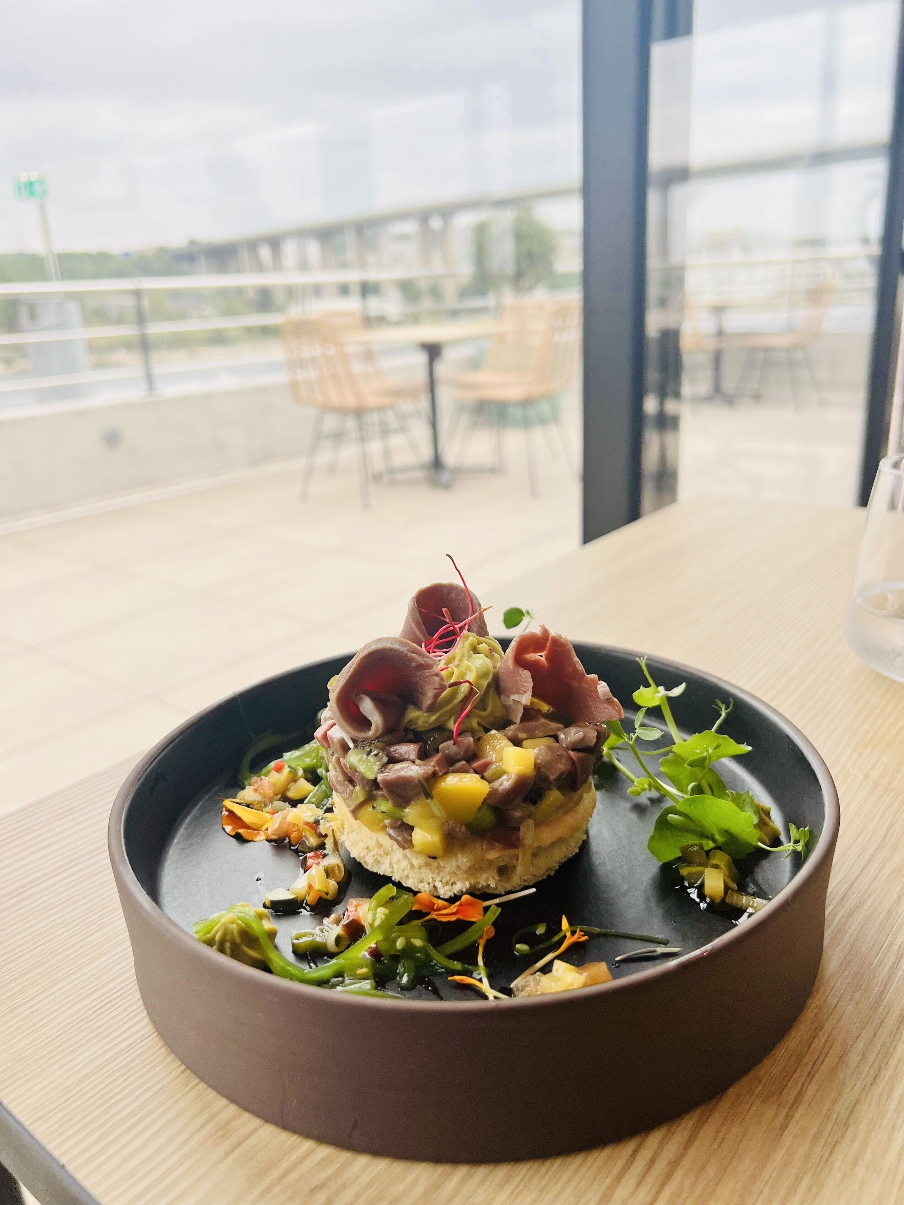 Un plato con diversos ingredientes, sobre una mesa con vistas a una terraza.