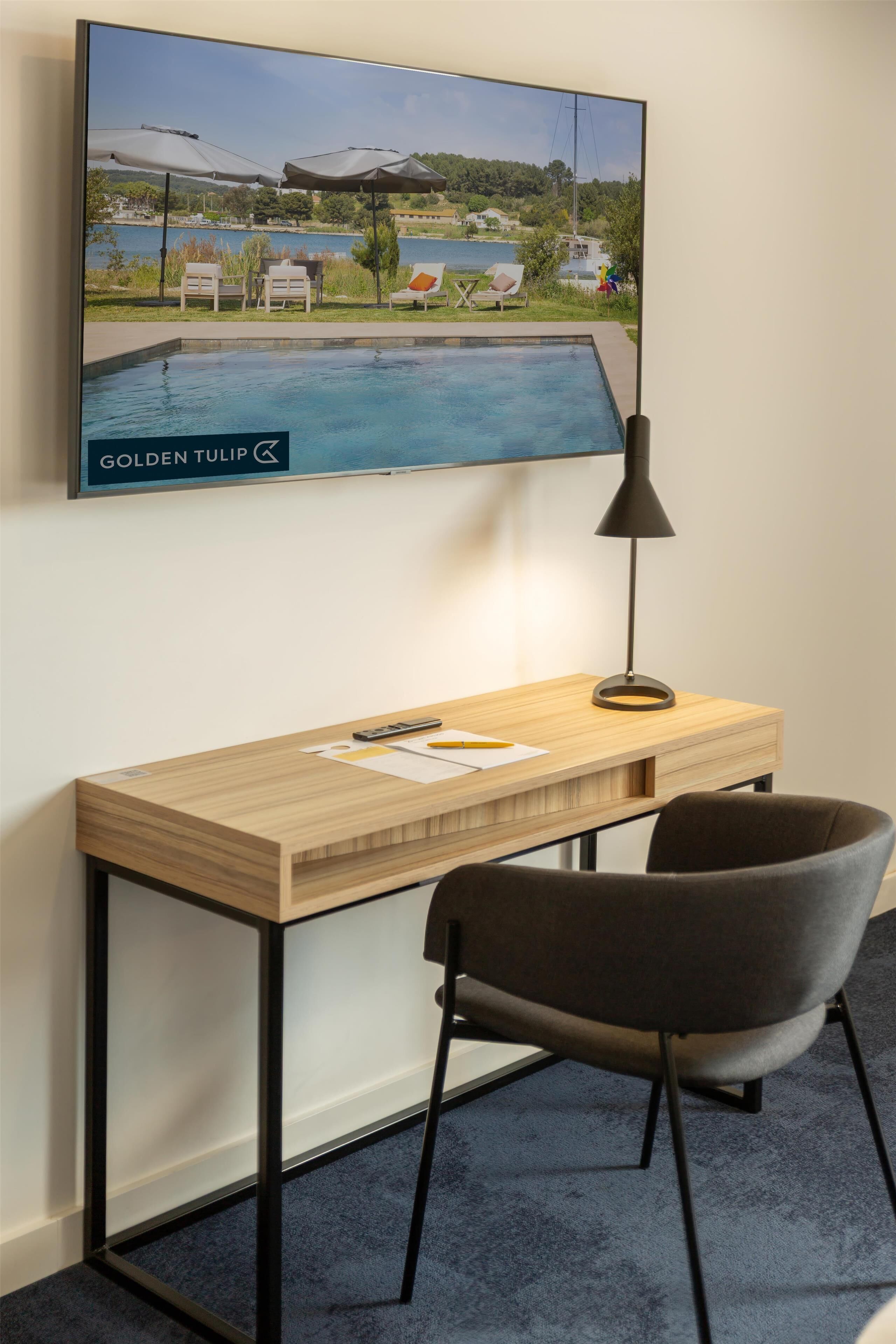 A modern workspace with a wooden desk, a black chair, and a TV displaying a pool view.