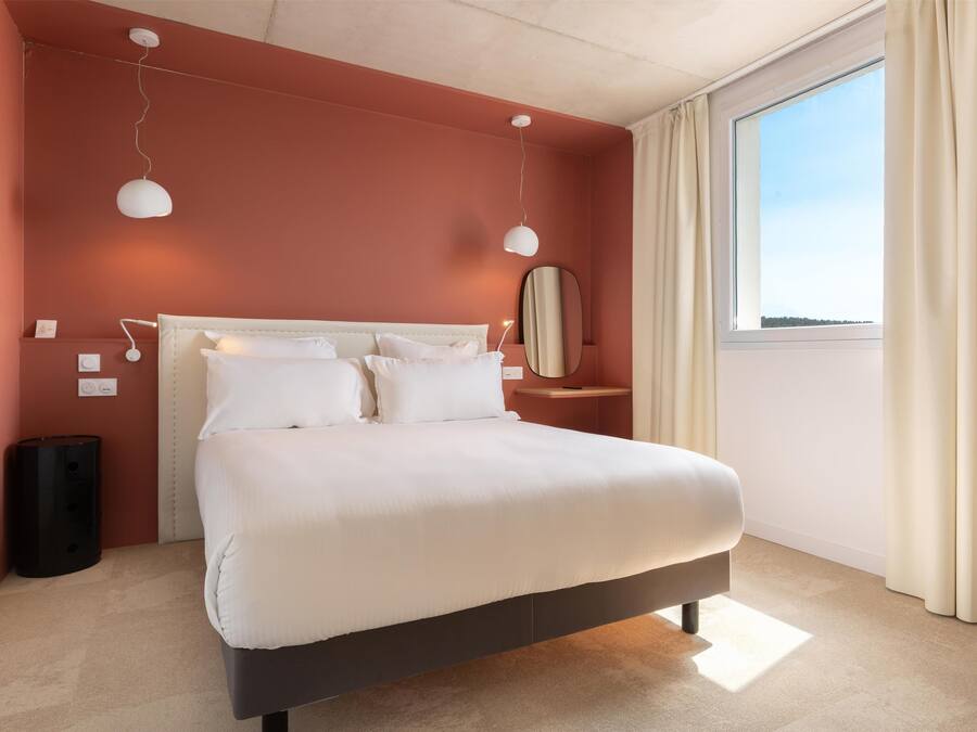 A modern bedroom with a large bed, bedside lamps, a nightstand, and a window with curtains.