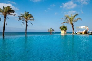 An infinity pool with palm trees and a beach view.