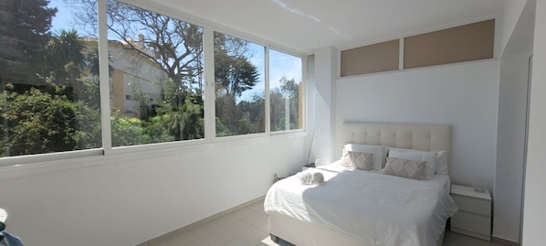 A bedroom with a large window, a bed with white bedding, and a small dog on the bed. - Beautiful apartment with a pool and air conditioning, near the Miraflores and Mijar golf courses (Mijas Costa)