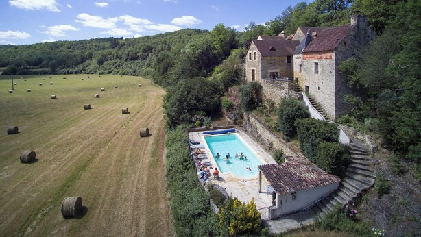 A stone building with a swimming pool and hay bales in the field.
