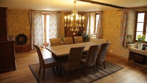 A dining room with a wooden table and wicker chairs, a chandelier, and floral curtains.