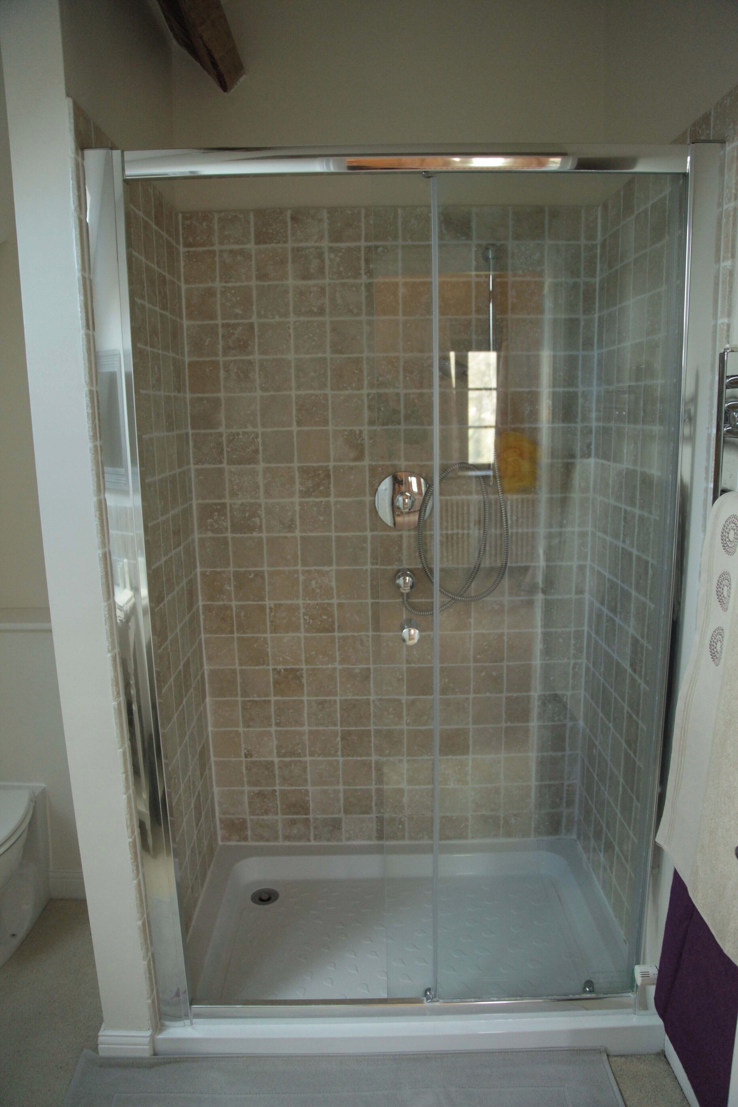 Una ducha a ras de suelo con puerta de vidrio, paredes de azulejos y ducha.