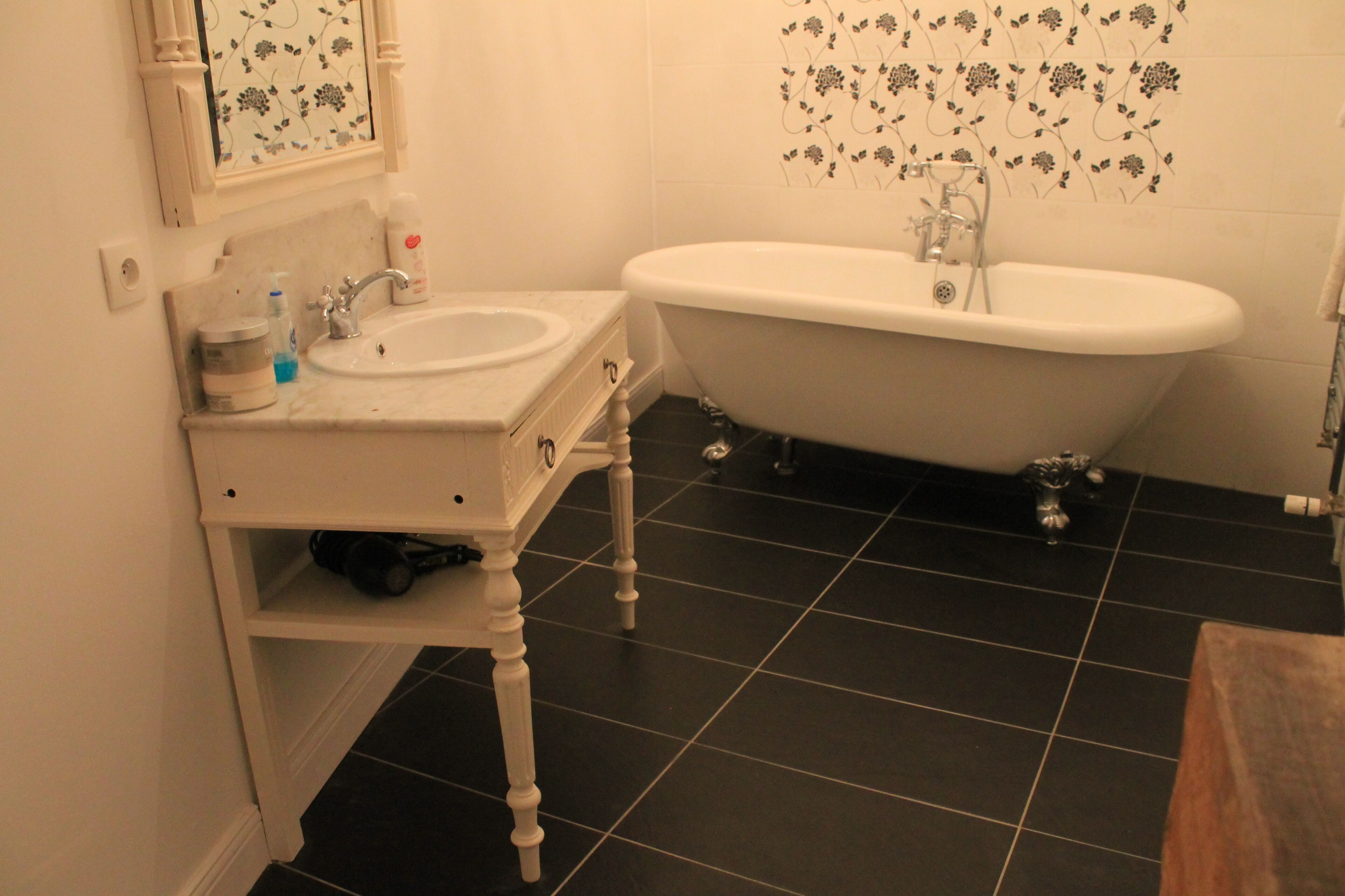 A bathroom with a white sink, a bathtub, and black tiled flooring.