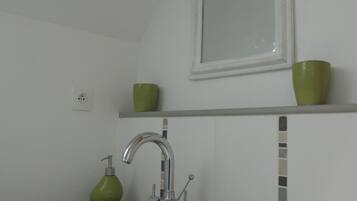 Un bagno con un lavandino bianco, un portasapone verde e uno specchio sopra il lavandino.
