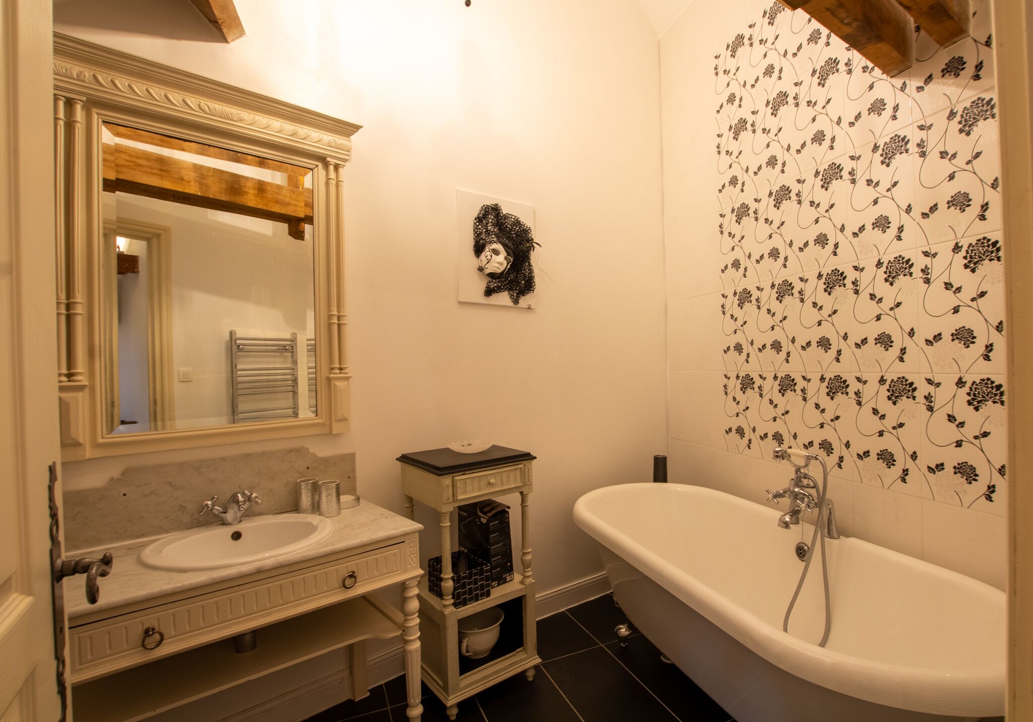 A bathroom with a white sink, a mirror with a wooden frame, a white bathtub, and a floral-patterned shower wall.