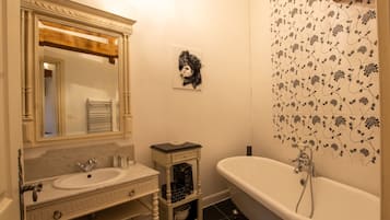 A bathroom with a white sink, a mirror with a wooden frame, a white bathtub, and a floral-patterned shower wall.