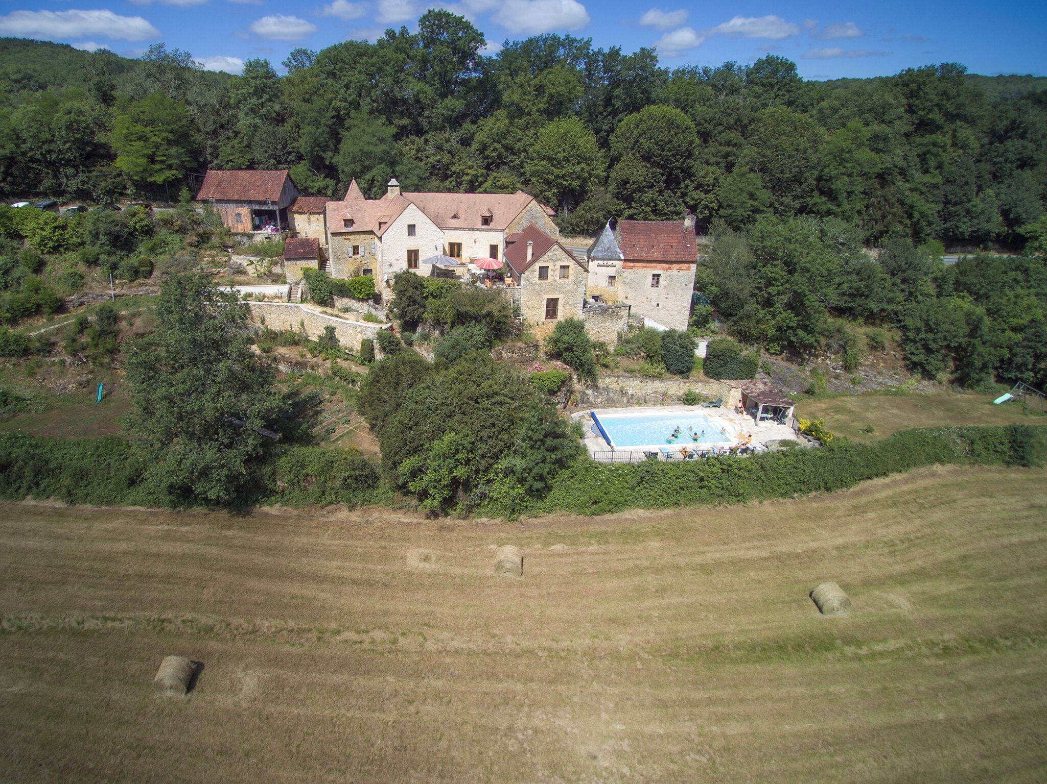 Un grand bâtiment en pierre comprenant de nombreuses pièces, une piscine et un jardin qui l’entoure.