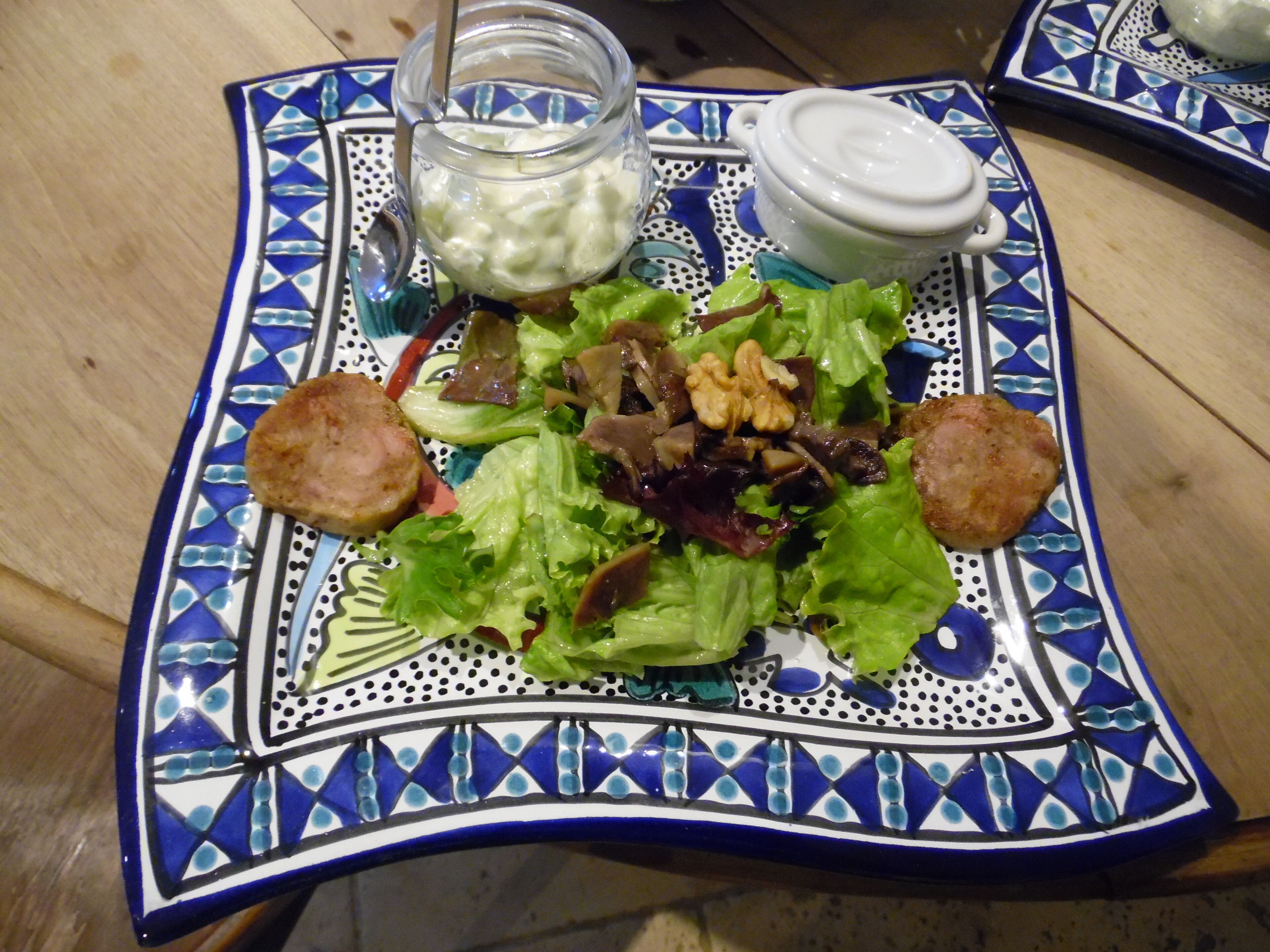 Ensalada con crutones y un frasco de aderezo sobre un plato decorativo azul y blanco.