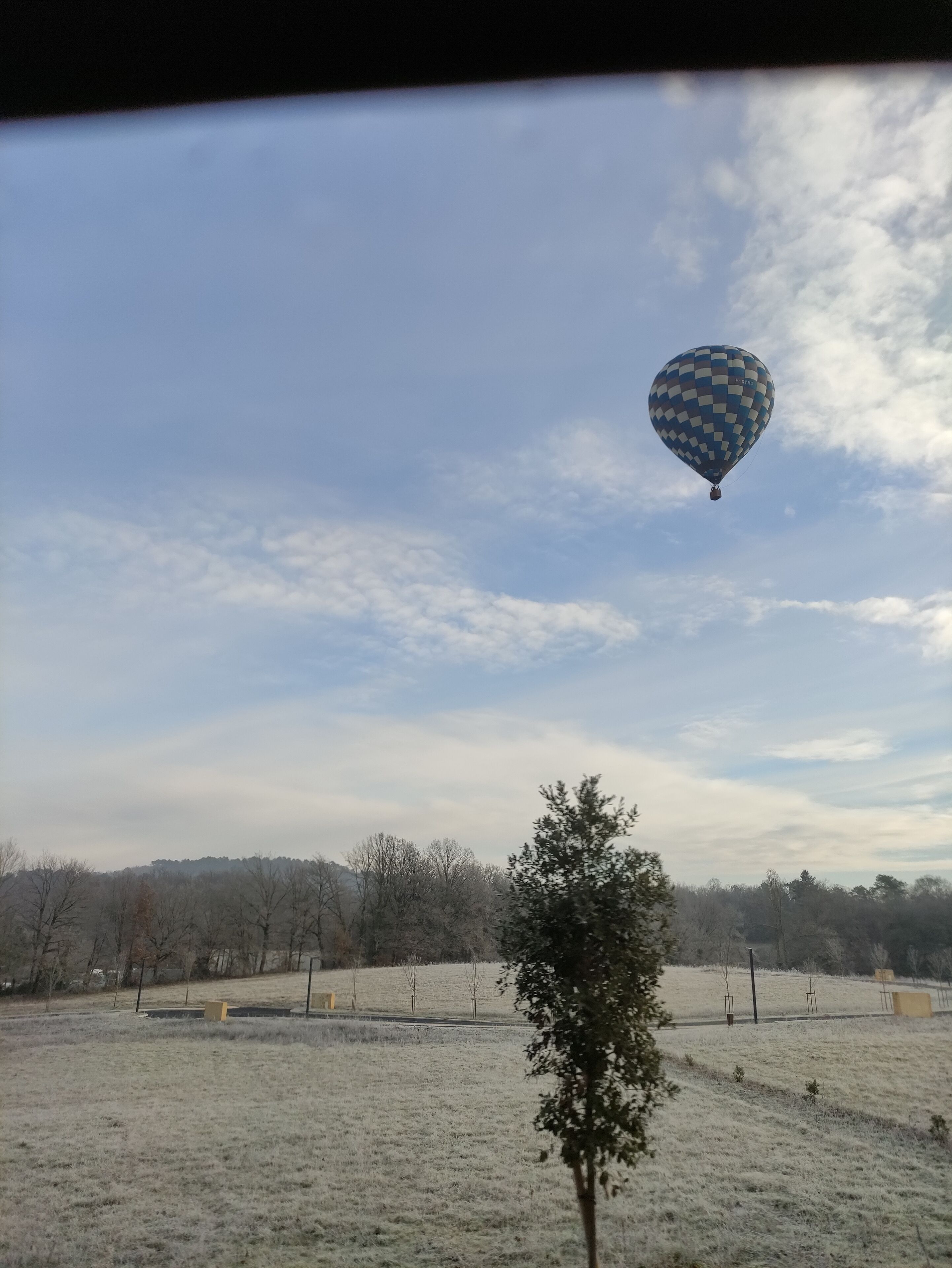 En varmluftsballong svävar över ett frostigt fält med kala träd och en klar himmel.