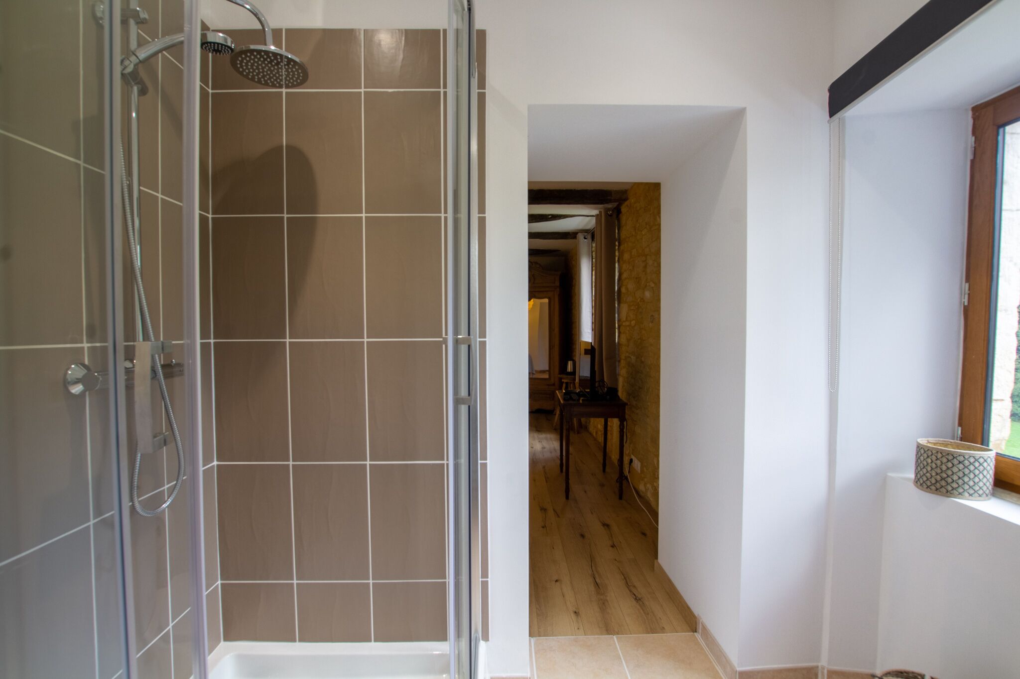 A shower with a glass door, a wooden floor, and a window with a view.