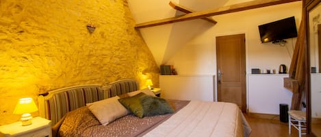 A bedroom with a stone wall, a bed with patterned bedding, a nightstand with a lamp, and a television mounted on the wall.
