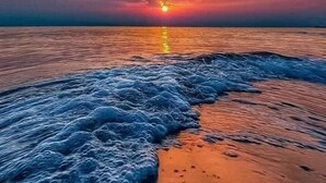 A beach with waves approaching the shore and a sunset in the background.