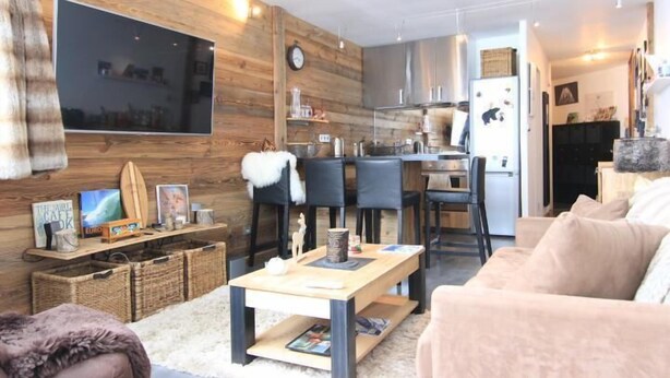 A modern living room with a large flat-screen TV, a wooden accent wall, a dining area with chairs, and a kitchen in the background. - 200m from ski slopes, 2nd floor, tv, 34m², Val Thorens (Val Thorens)