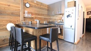 A modern kitchen with wooden paneling, a central island with bar stools, stainless steel appliances, and a clock on the wall. - 200m from ski slopes, 2nd floor, tv, 34m², Val Thorens (Val Thorens)