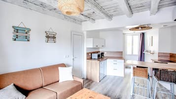 A modern interior with a sofa, a wooden table, a kitchen area with cabinets and a microwave, and a hanging light fixture.