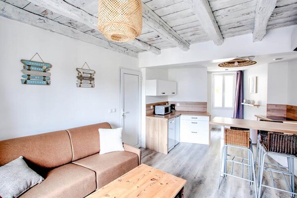 A modern interior with a sofa, a wooden table, a kitchen area with cabinets and a microwave, and a hanging light fixture.