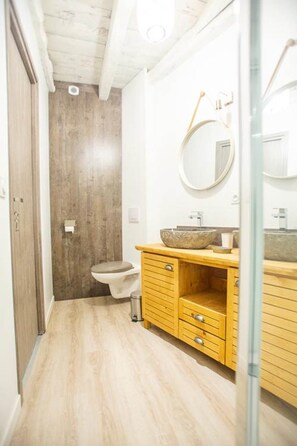 Ein Badezimmer mit einem Holzkosmetikschrank, einem runden Spiegel und einer Toilette.