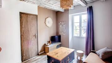 A room with a wooden door, a television on a stand, a small table, a sofa, and a window with curtains.