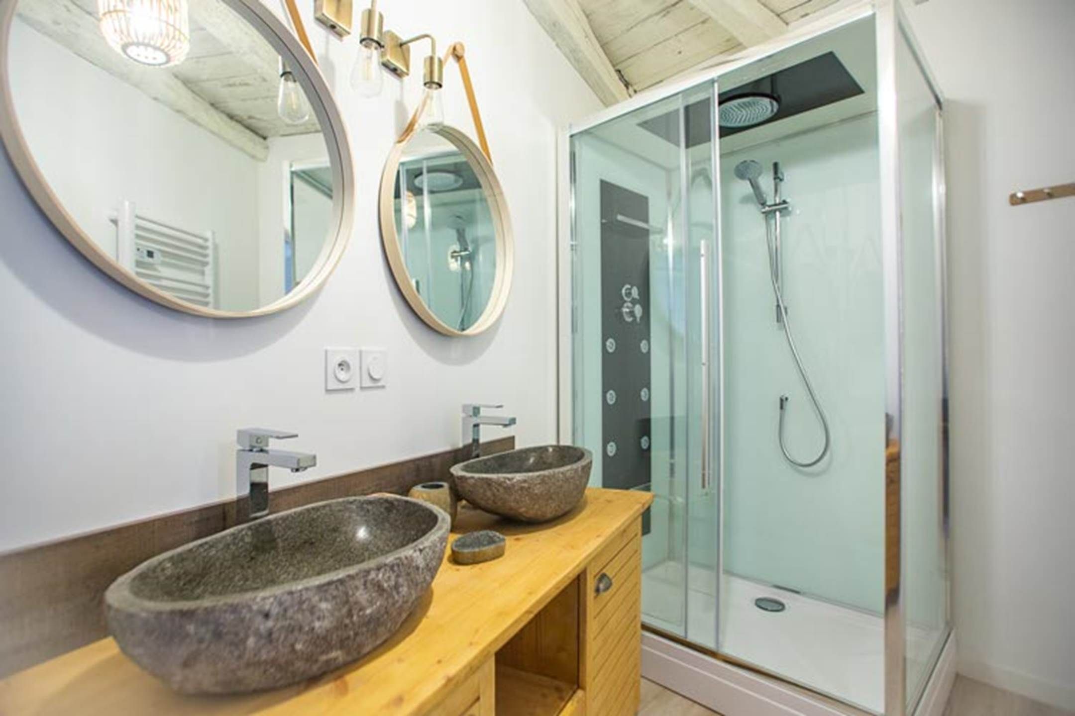 Une salle de bain avec deux miroirs ronds, un lavabo en granit et une douche à parois de verre.