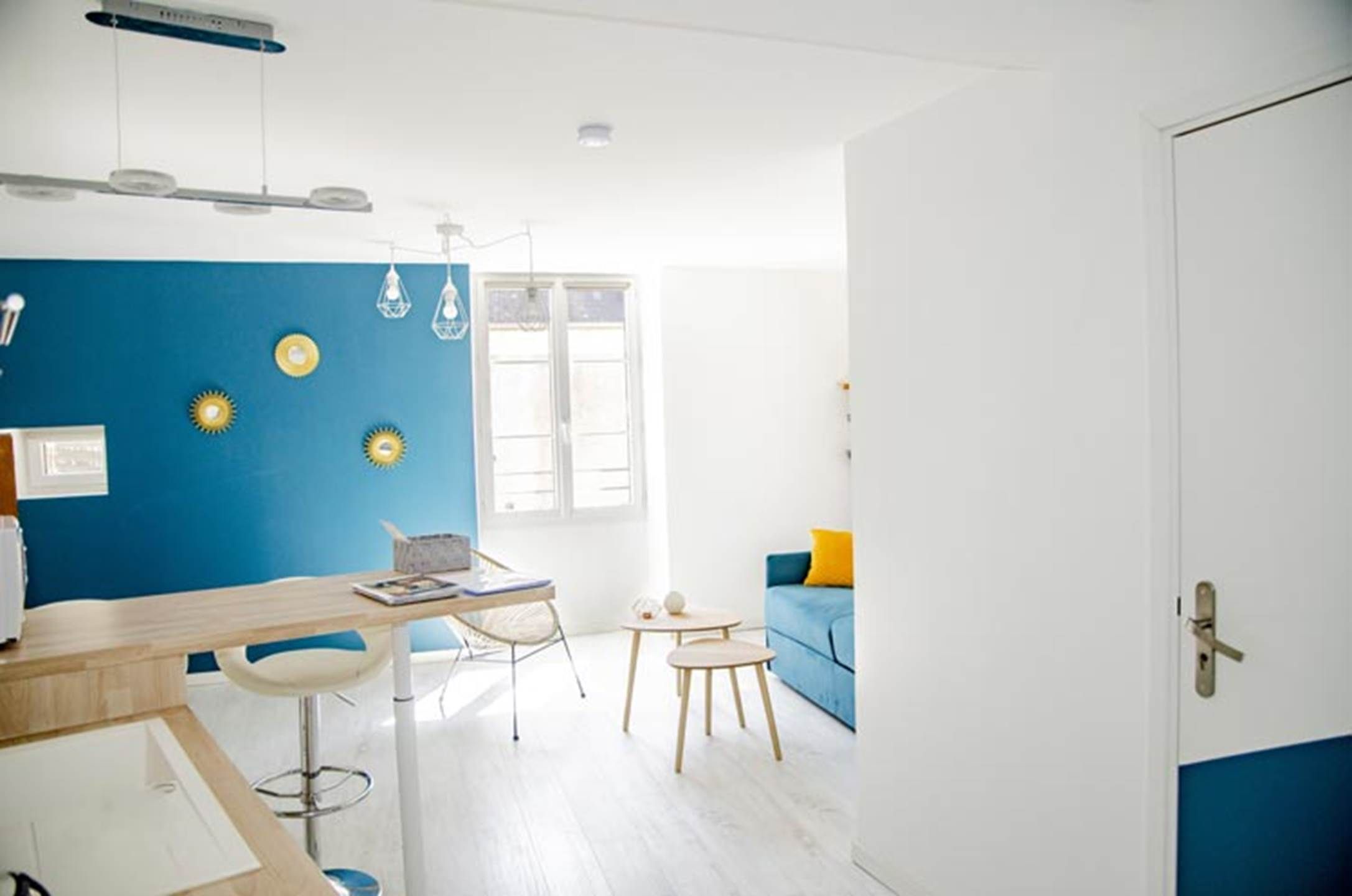 Une pièce moderne avec un mur d’accent bleu, un bureau en bois, une petite table ronde, un canapé bleu et une porte blanche.