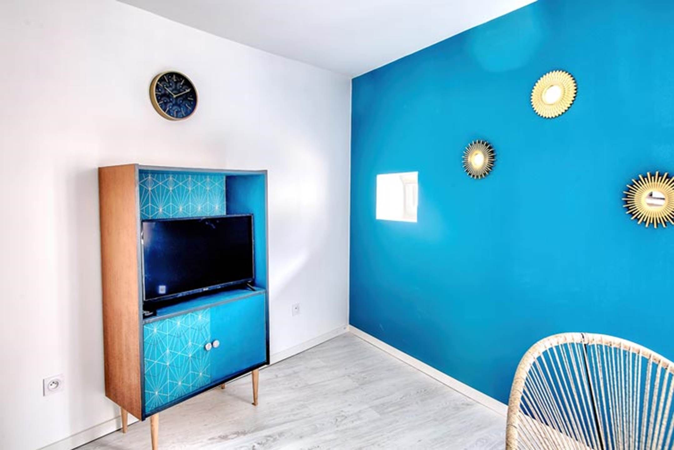 Een kamer met een blauwe wand, een houten kast met een televisie en een stoel.