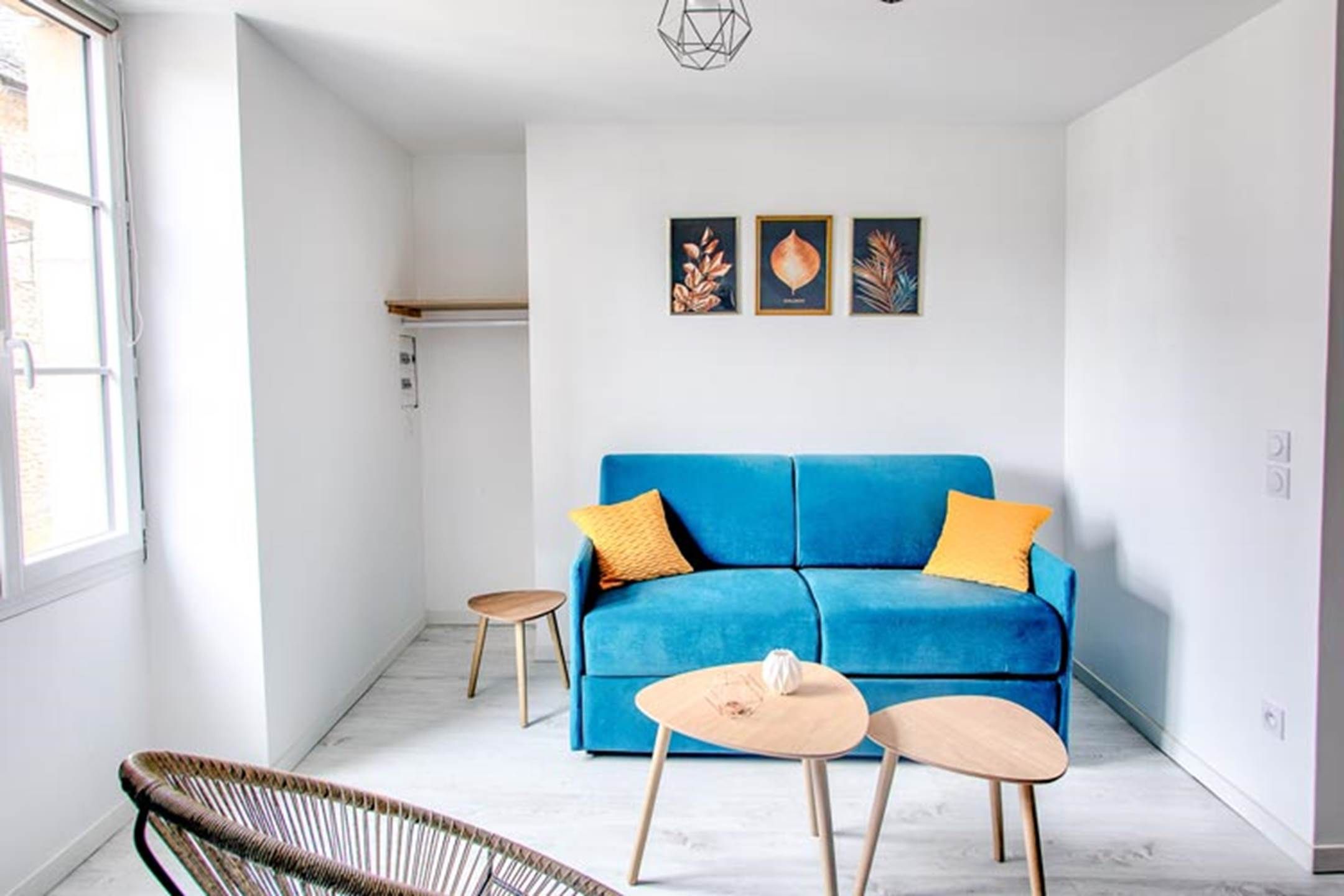 Een moderne woonkamer met een blauwe bank, twee kleine tafels en een rieten stoel.