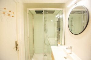 A modern bathroom with a glass-enclosed shower, a white sink, and a round mirror.
